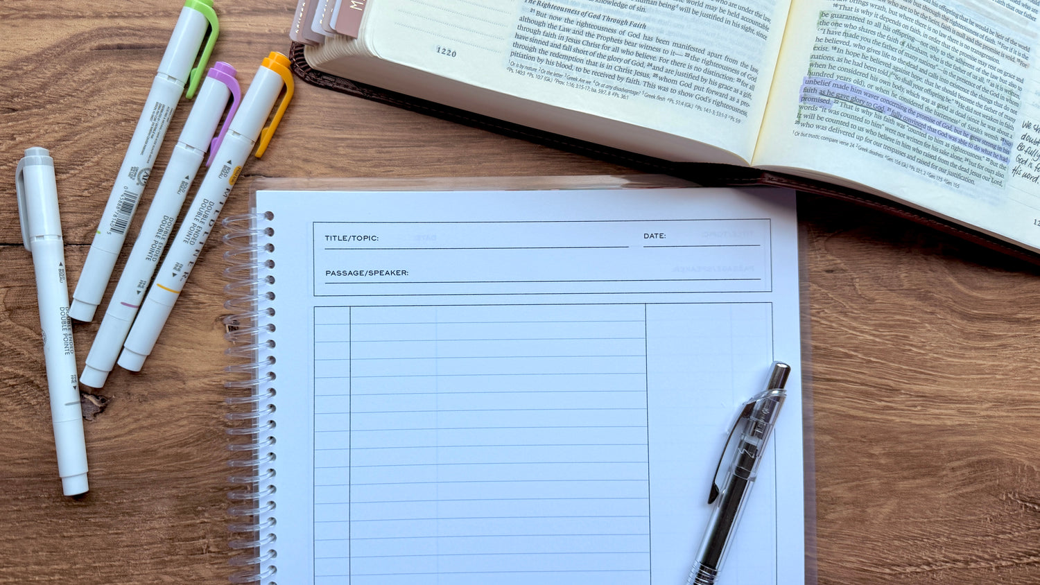 Notebook with planner pages, markers, and an open book on a wooden surface