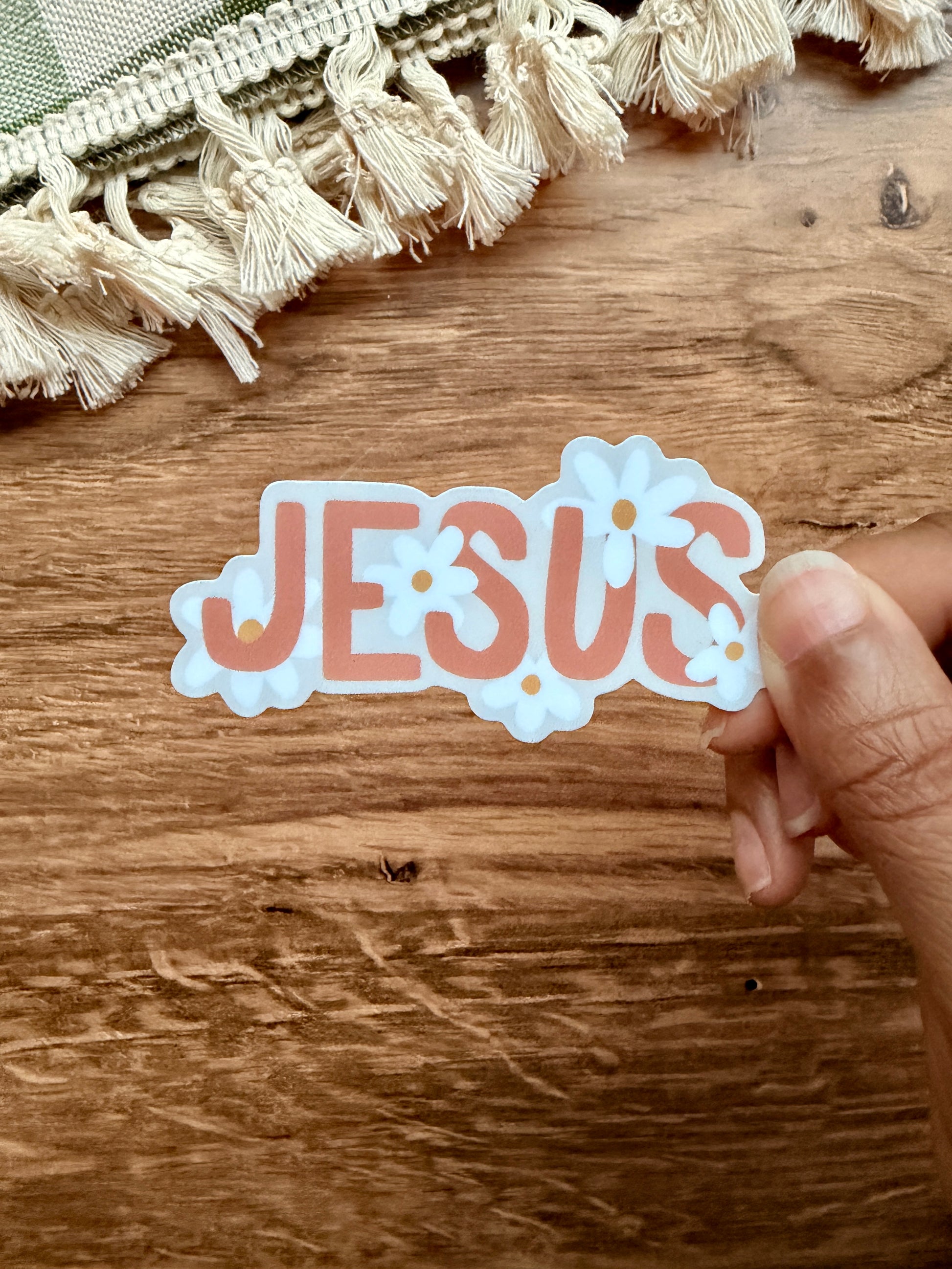Jesus Floral Daisy Sticker with colorful lettering and floral designs on a wooden surface.